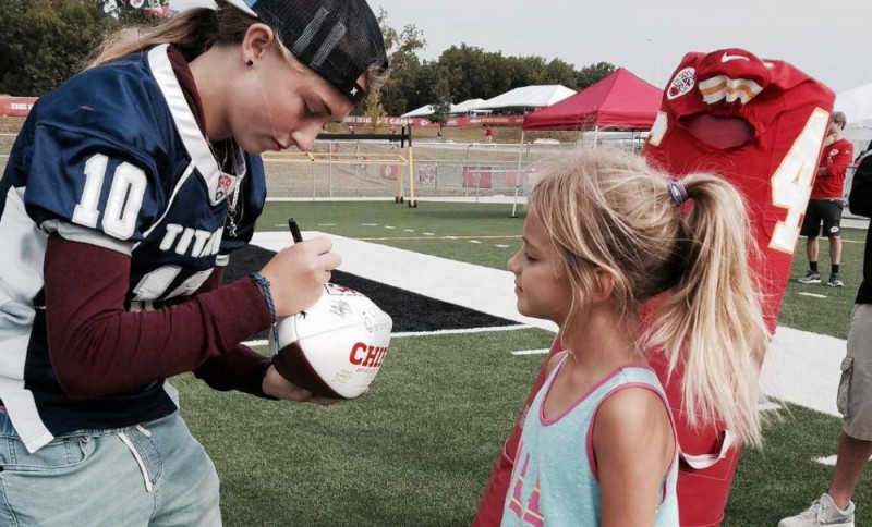 Teen girl who was high school quarterback signs football for little girl 