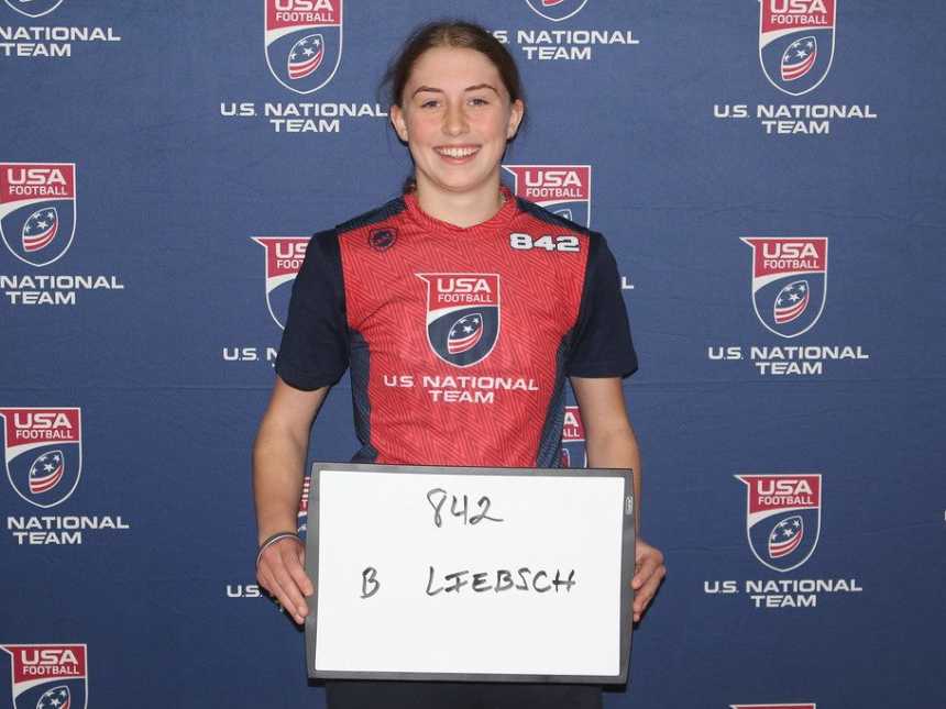 Teen girl stands holding whiteboard in front of backdrop that says, "US National Team"