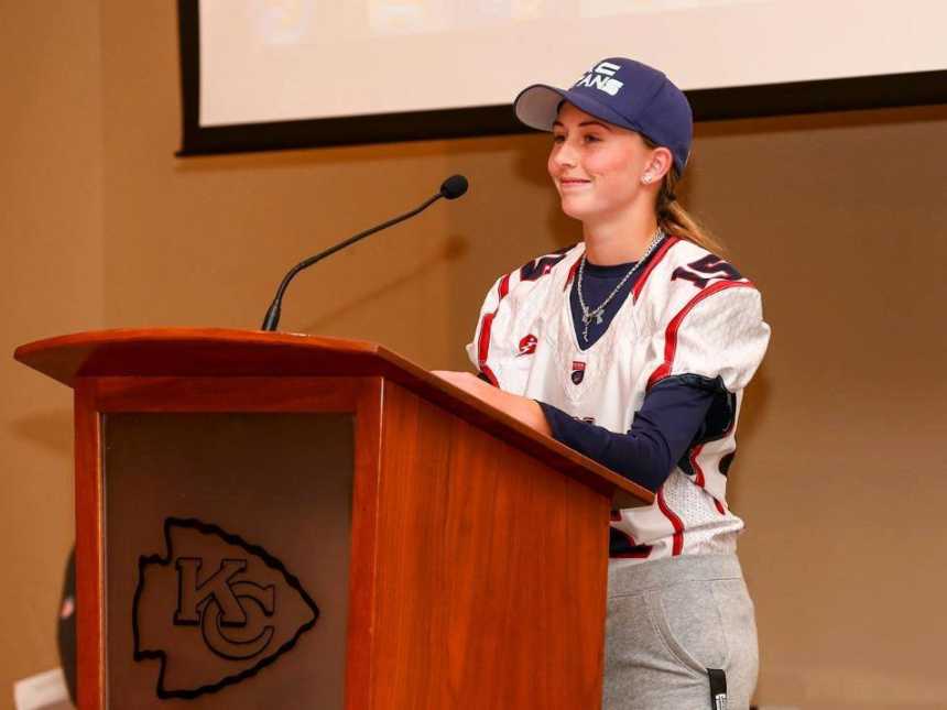 Teen girl stands at Kansas City Chiefs podium wearing football jersey