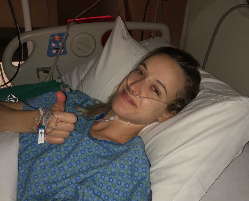 Woman who fell off of her horse lays in hospital bed with thumbs up