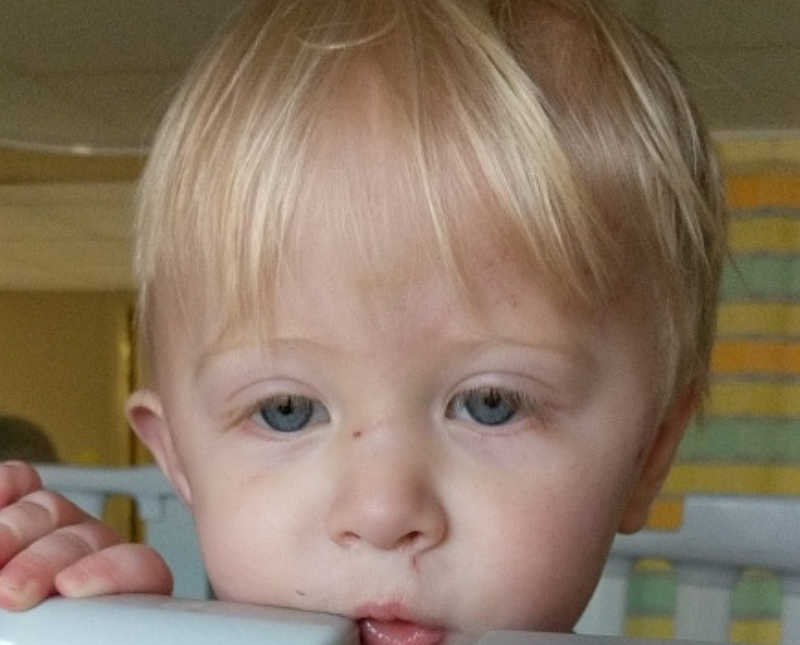 Close up of little boy's face who rests his head on side of crib