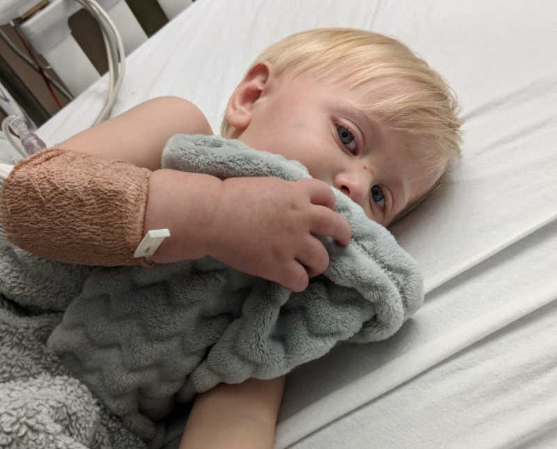 Little boy lays in hospital crib snuggling with fuzzy blanket