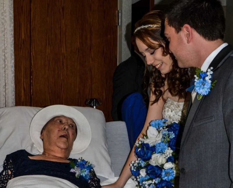 Bride stands beside groom and grandmother who lays in hospital bed with lung cancer