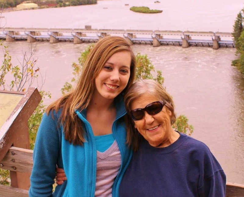 Young woman stands beside grandmother in front of body of water
