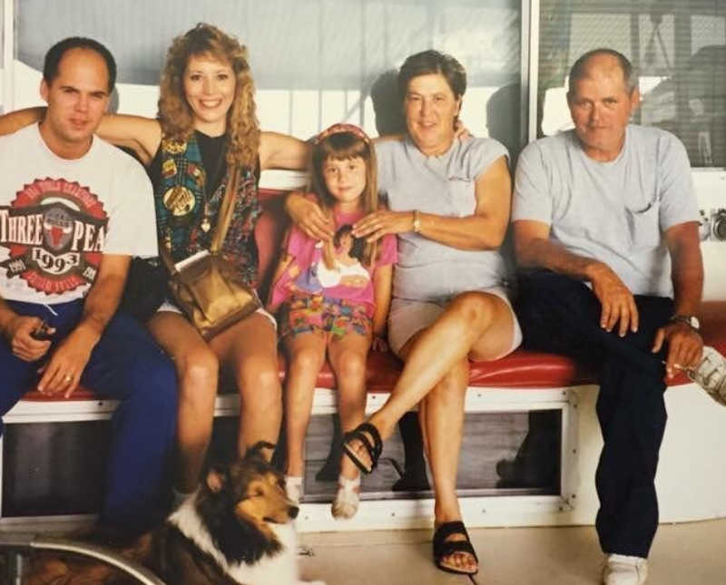 Little girl sits on bench beside her parents and grandparents 