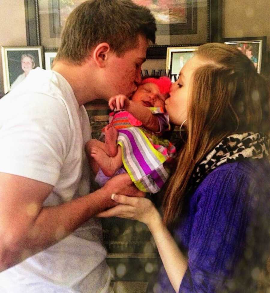 Teen parents hold newborn as they kiss each of her cheek