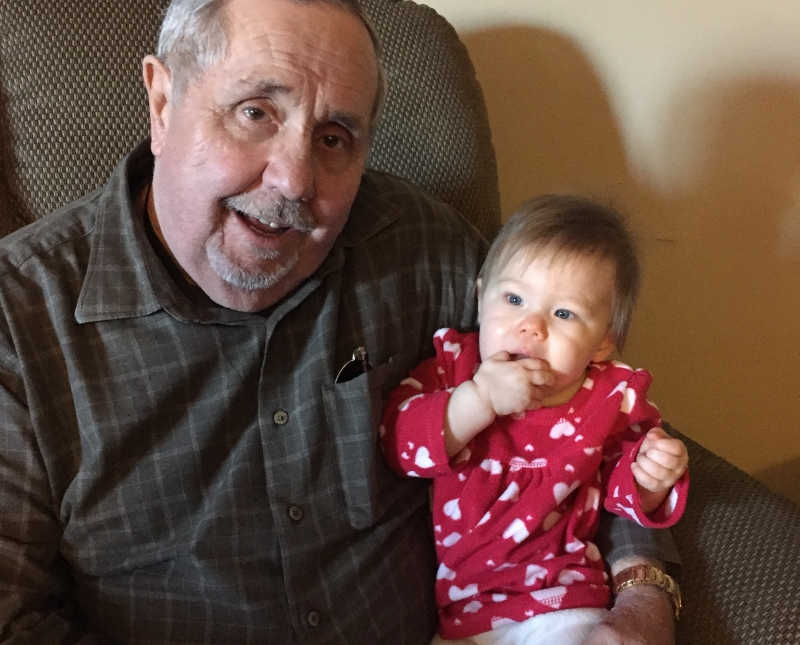 Man sits in chair with granddaughter in his lap