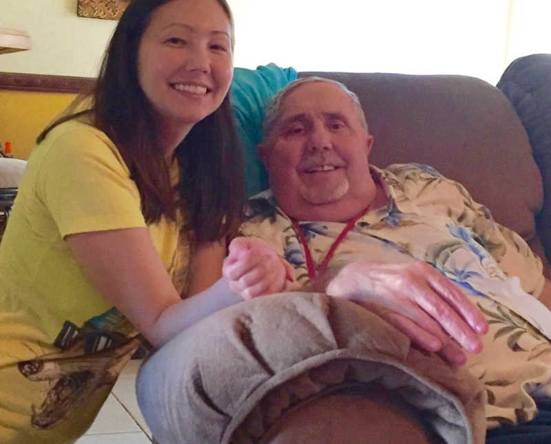 Woman kneels beside father with stage IV cancer who sits in chair
