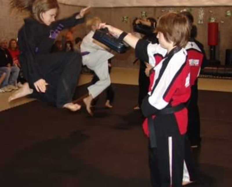Teen girl jumps in air at karate as boy holds up pad for her to kick
