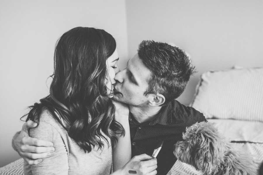 Husband and wife who miscarried baby sit on bed kissing each other