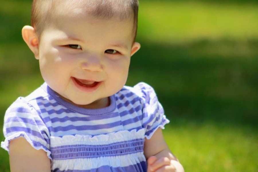 Baby girl smiles as she wears a purple and white stripe dress