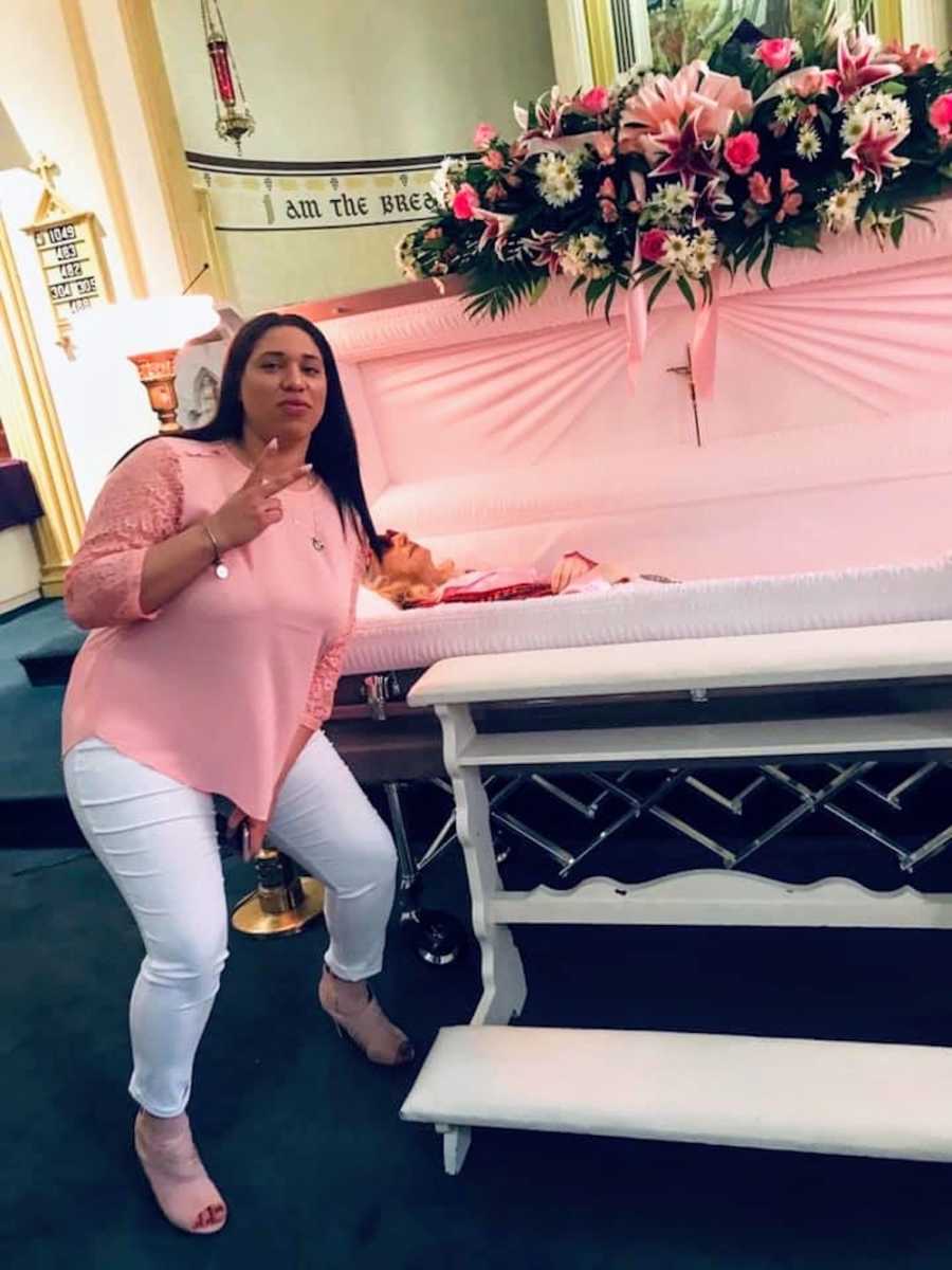 Woman holds up peace sign beside grandmother's open casket