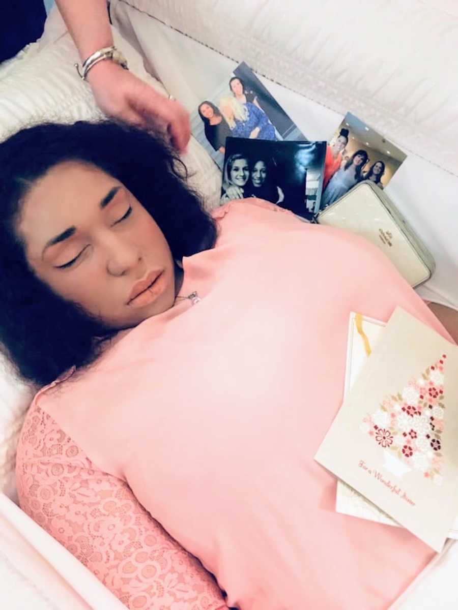 Deceased woman lays in casket with pictures beside her and card on her chest