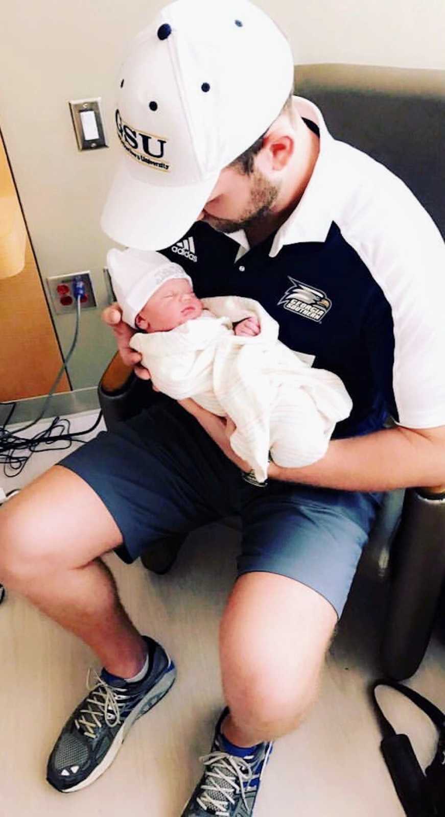 Father sits in hospital room holding newborn in his arms