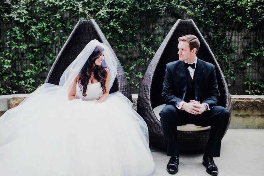Bride and groom sit beside each other outside in modern chairs