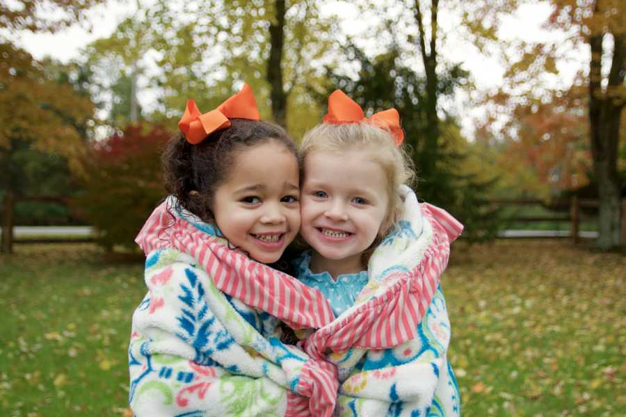 Sisters stand in yard smiling with blanket wrapped around them