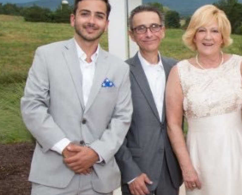 Young man who has since passed stands outside in formal attire beside his parents