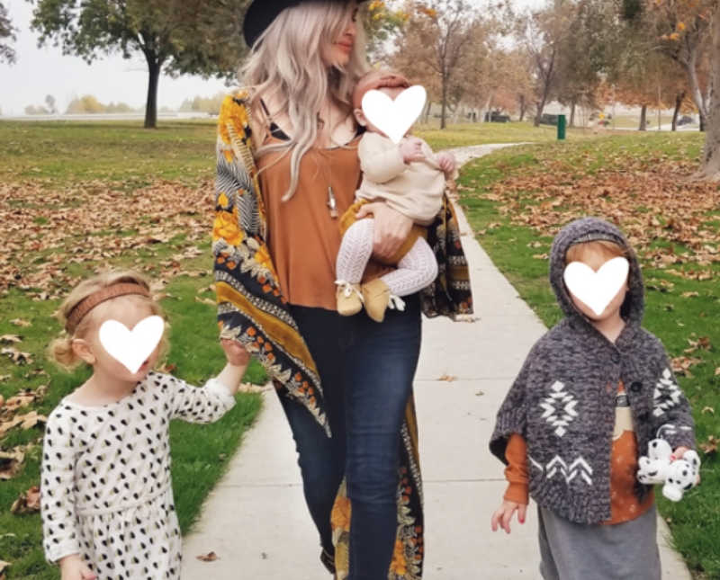 Foster mother walks on sidewalk holding baby while two young girls walk beside her