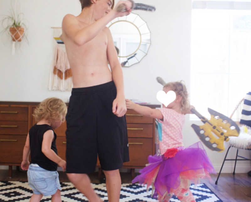 Oldest foster child stands in living room of home playing with two youngest foster sisters