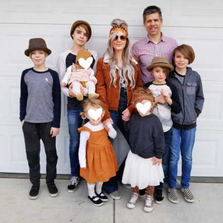 Foster parents stand outside in front of garage door with their seven foster kids