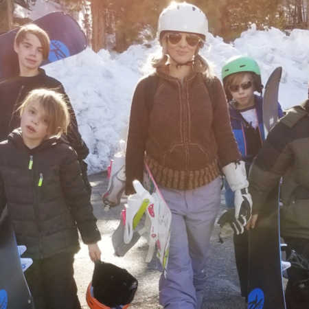 Mother stands outside holding snowboard with three foster sons
