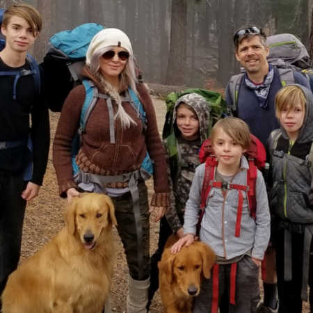 Husband and wife stand outside with their two dogs and four foster sons