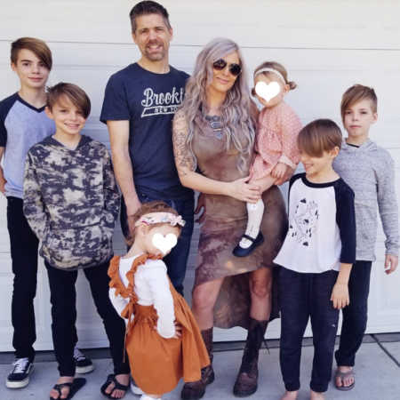 Husband and wife stand outside in front of their garage door with their six foster kids