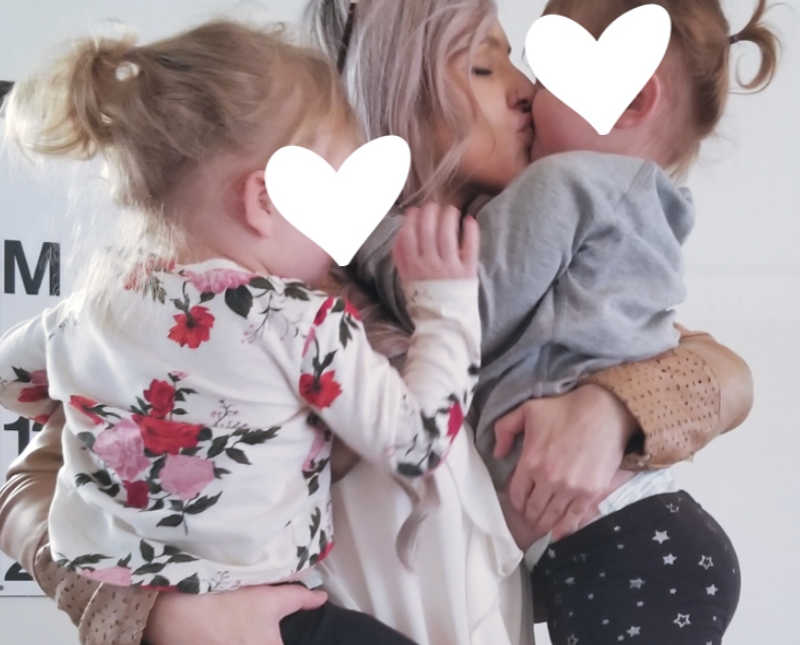 Foster mother holds two young daughters as she kisses one on her cheek