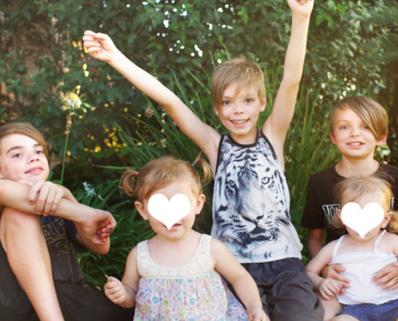Five foster kids sit outside smiling while youngest two have white hearts photoshopped over their face