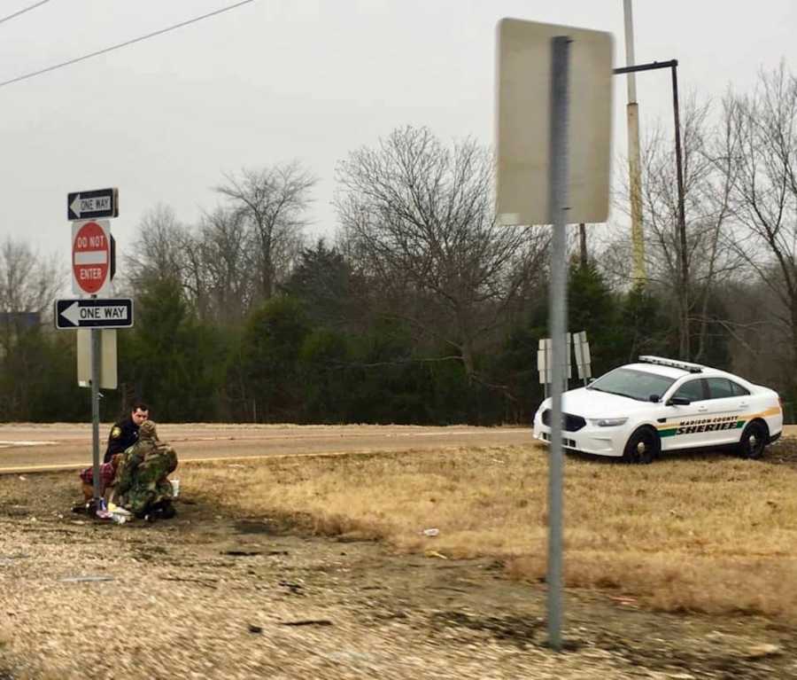 Policeman crouches down beside homeless man on side of road to offer him lunch