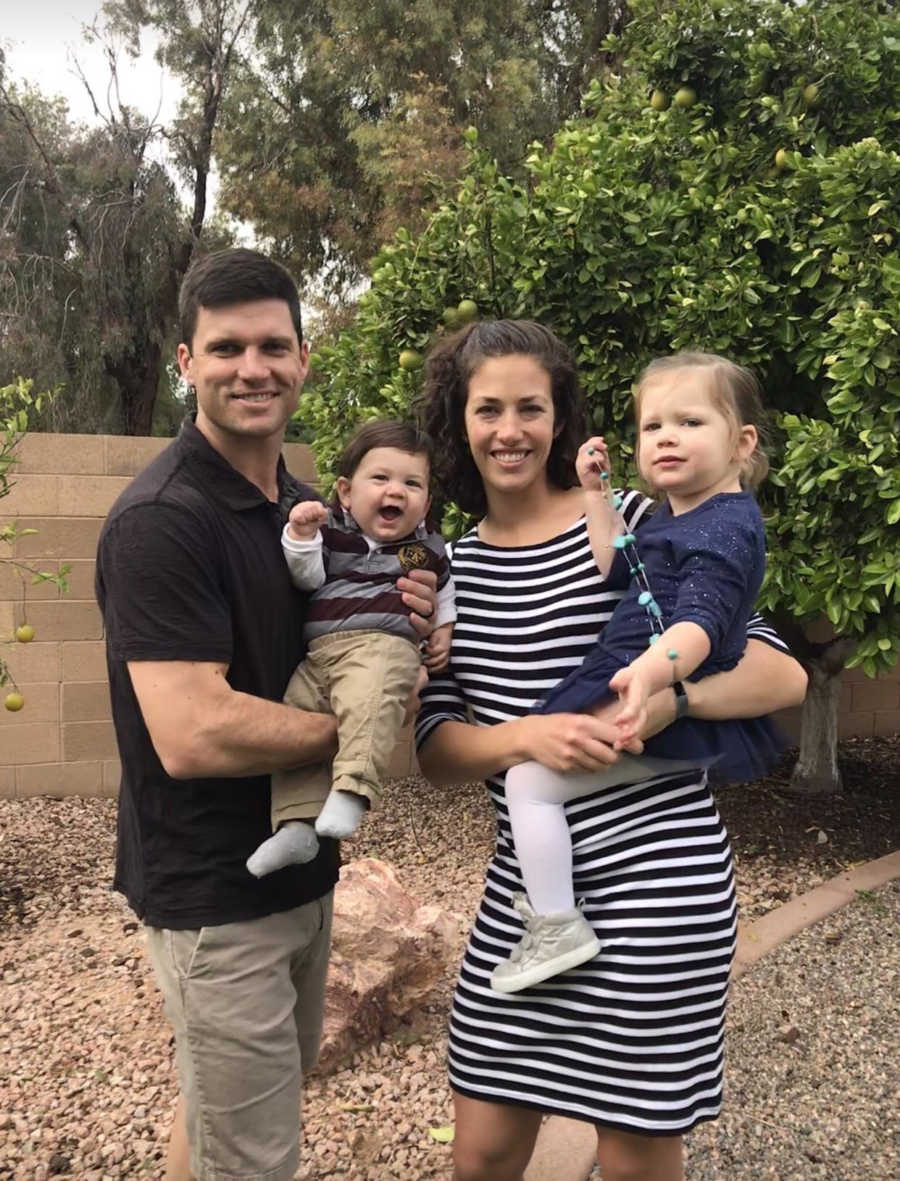 Husband and wife stand outside holding their son and daughter