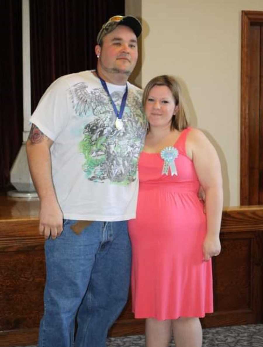 Pregnant woman stands smiling arm in arm with her husband