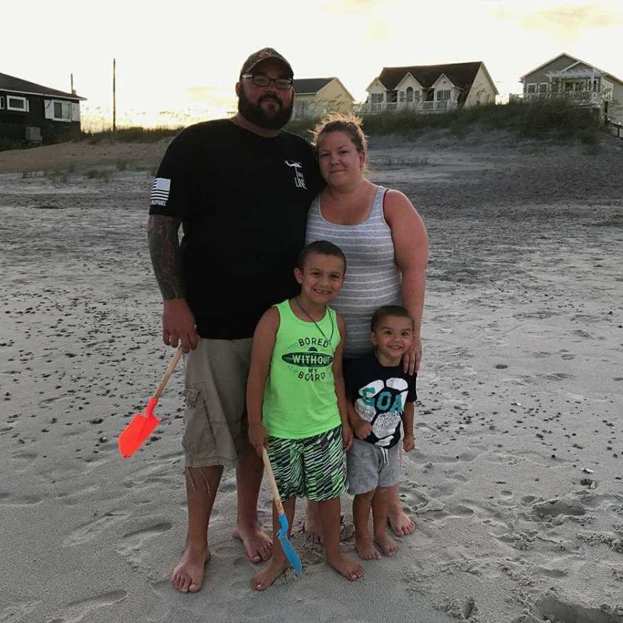 Husband and wife stand on beach with their two young sons