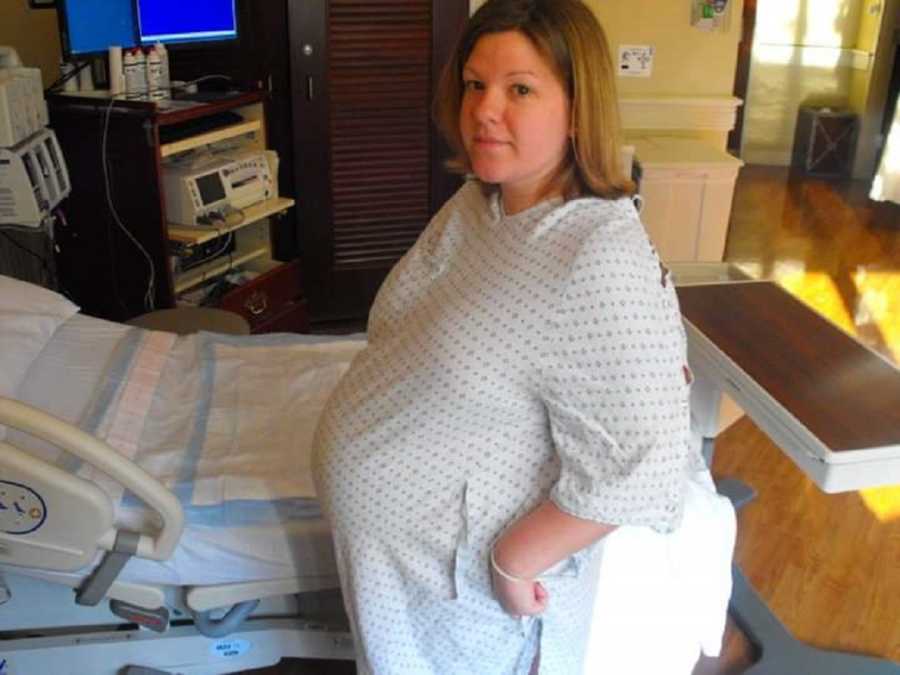 Pregnant woman stands in hospital room beside bed