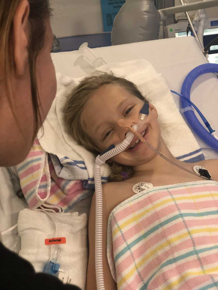 Little girl who almost died lays smiling in hospital bed with tube up her nose