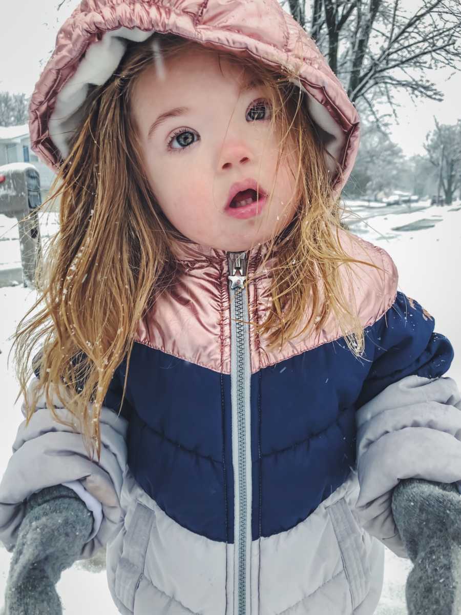 Little girl with down syndrome stands outside in winter clothes