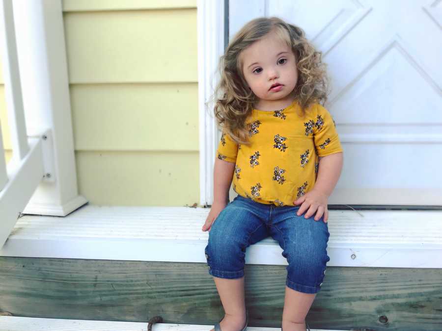 Little girl with down syndrome sits on steps outside her home