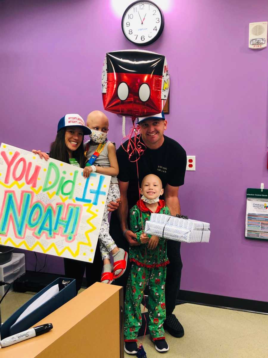 Mother holds son who completed chemo and holds sign for him beside husband and daughter with brain cancer