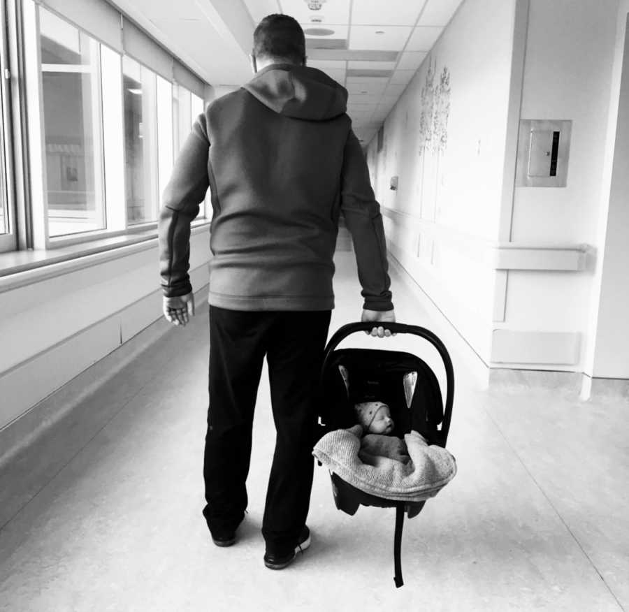 Father walks down hospital hallway carrying newborn in carseat 
