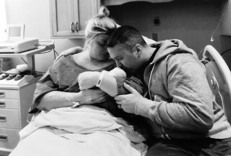 Husband and wife who just gave birth sit in hospital bed holding their stillborn 