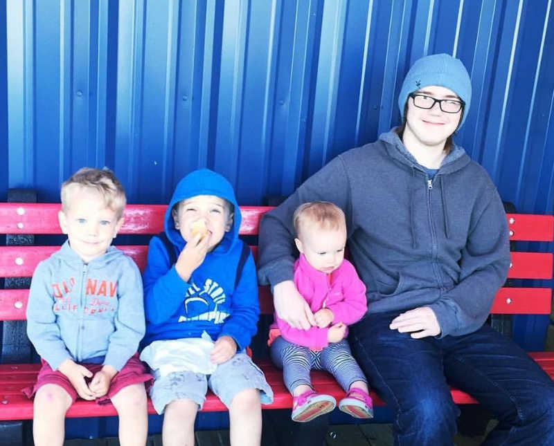 Teen sits on bench beside three young kids