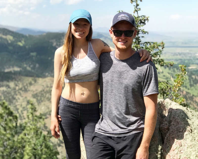 Young woman with autoimmune disease stands with arm around boyfriend on hike