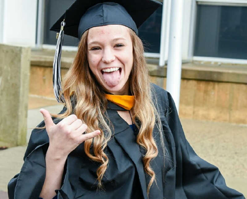 Young woman in cap and gown sticks tongue out and holds up shaka sign with hand