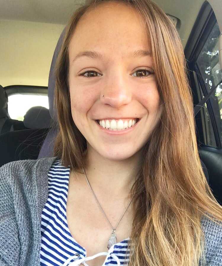 Young woman with autoimmune disease smiles as she sits in car taking selfie