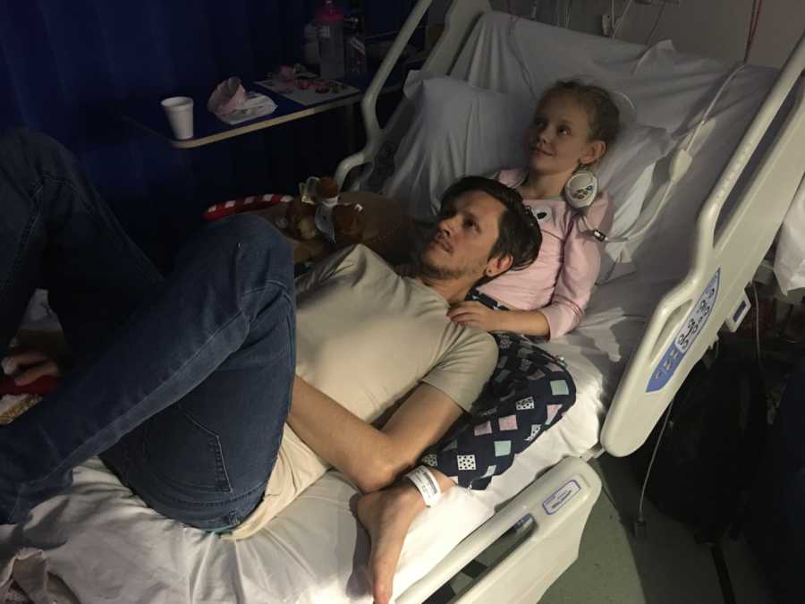 Young girl with rhinovirus lays in hospital bed with father