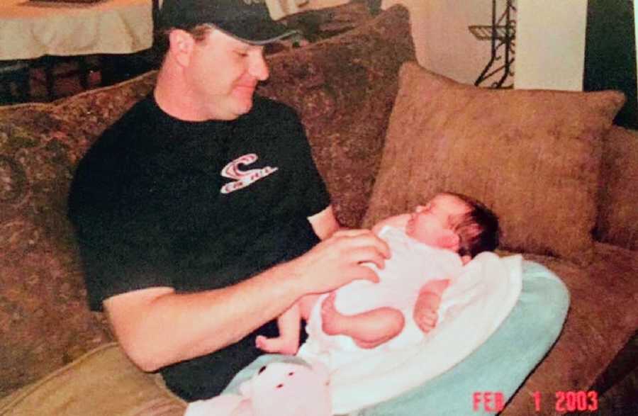 Father sits on couch with baby daughter sleeping on his lap