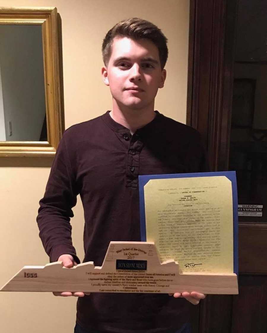 Teen who just graduated high school and will join the Navy stands holding certificate and wooden trophy