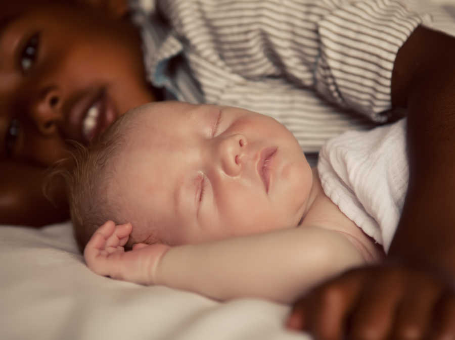 African American boy lays with arm around white baby brother who lays sleeping