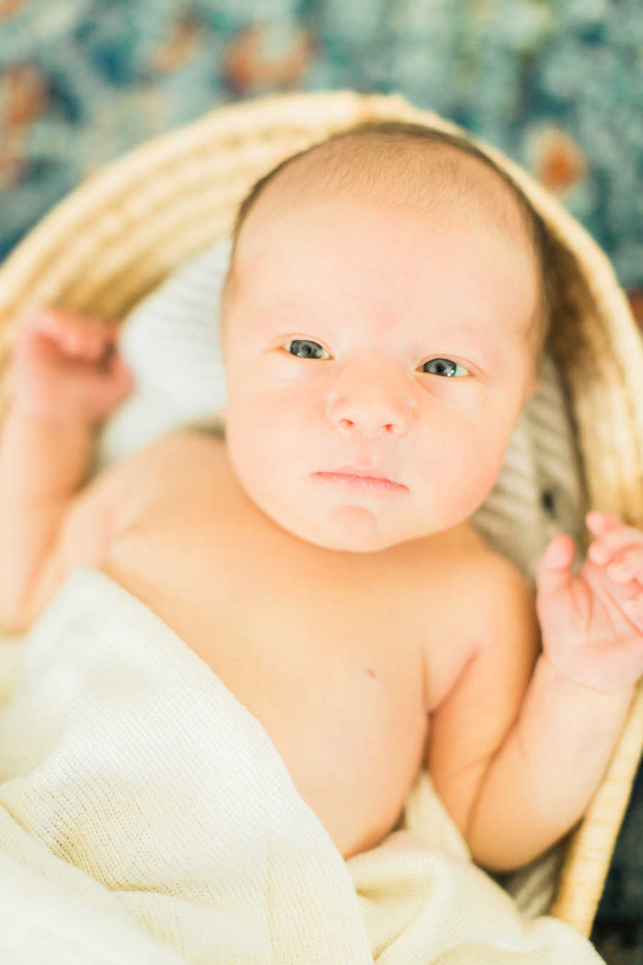 Adopted baby lays on his back in basket for photoshoot