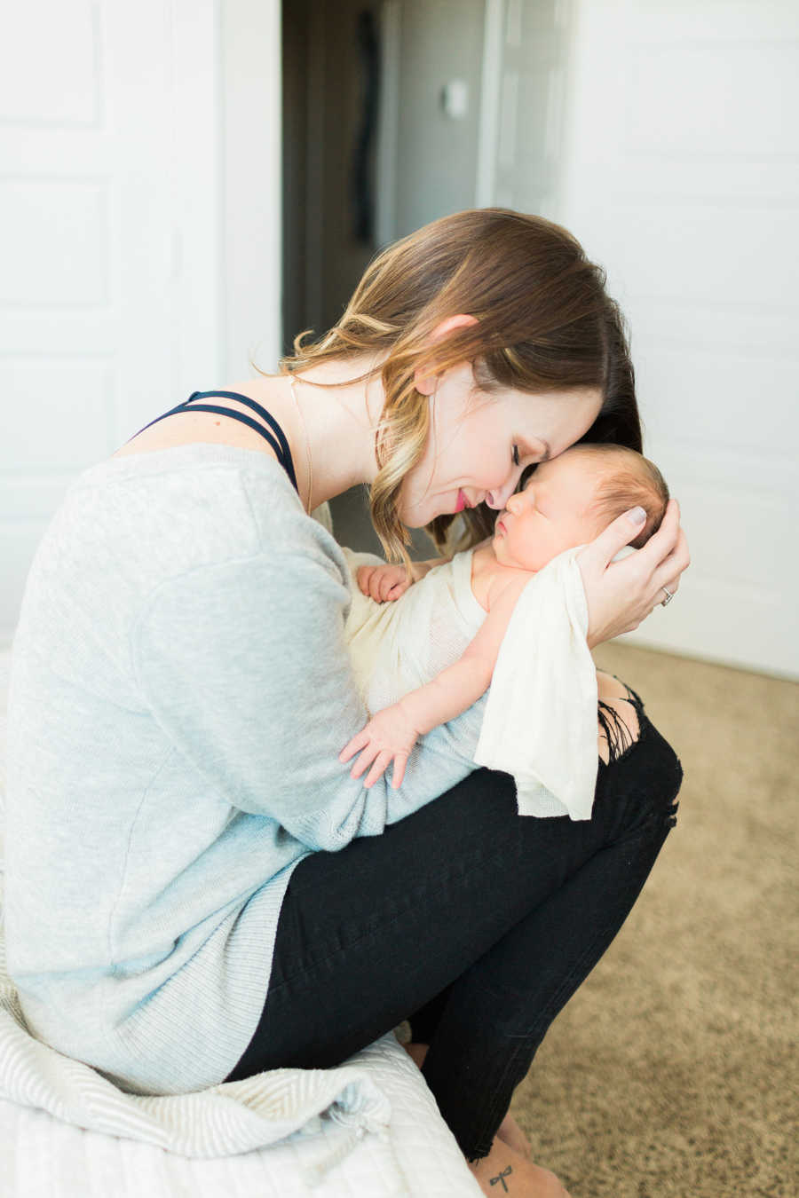 Mother sits on edge of bed holding adopted newborn close to her face